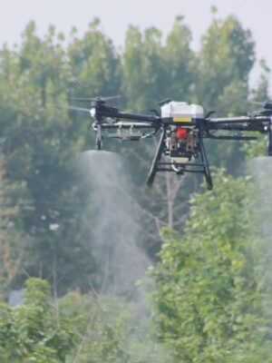 A professional DJI Agras T40 agricultural drone in mid-air flight spraying crops over a green field, highlighting its coaxial twin-rotor setup and payload tank configuration for commercial buyers checking the price.